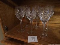 Set of six Marquis by Waterford crystal wine glasses displayed together on wooden shelf.
