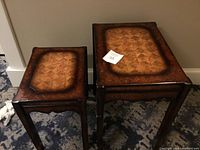 Two wooden nesting tables of different sizes with decorative top pattern, placed on carpet, showing overall condition including wear and finish.