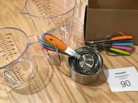 Photo of metal measuring spoons with colorful handles nested on a ring and metal measuring cups with similar colorful handles, plus a large clear plastic liquid measuring cup.