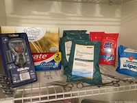 Photo shows the packaged Gillette Fusion razor, Colgate toothpaste, Scotties tissues box, Stryker shampoo caps, Wet Ones hand wipes, flushable moist wipes, and metal scissors lined up on a shelf.