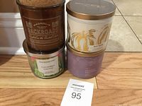 Four scented candles grouped on floor showing branding and labels: Magnolia Backroads, White Barn White Pumpkin and Cuddle Weather, Huntington Home Cucumber Cactus.