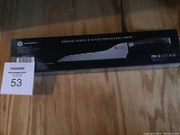 Photo of the entire boxed Kessaku Samurai Series 8-inch offset bread and deli knife on a wooden floor