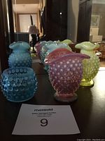 Photo showing 5 small hobnail glass vases in blue, yellow, and pink colors with hobnail textured pattern and ruffled rims, displayed together on a surface.