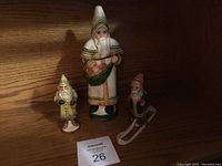 Three Vaillancourt Folk Art Father Christmas figurines on wooden shelf, including one large standing, one small standing, and one skiing figure