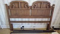 Front view of wooden bed headboard with carved decorative panels and side rails positioned behind it.