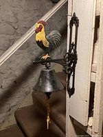 Side view of the cast iron bell mounted on a wall with a colorful rooster figure above the bell.