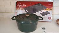 Green cast iron covered pot with metal knob lid in front of Lagostina grill box.