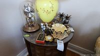 Full view of the anniversary clock, abacus, animal figurines including brass lady and silver cat, pineapple brass containers, bowl with brass top, mini apple picture frames, candle holder, and decorative sword picks arranged on a dark wooden table.