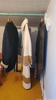 Three coats hanging on a rack: navy wool jacket, cream wool long coat, and brown leather jacket