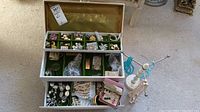 Wide angle photo showing open jewelry box with various costume jewelry pieces arranged inside compartments, a white necklace display stand with pearl and blue necklaces attached.