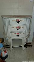 Front view of white painted demilune table showing the three drawers with floral hand-painted design and metal handles.
