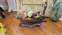 Side angled view of metal gondola holding faux fruits and vegetables on wooden floor with beige couch background
