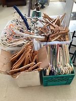 Overview of multiple boxes and crates filled with various types of clothes hangers: wooden, plastic, and wire.