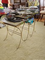 Side angle view of metal and glass nesting tables showing curved legs and glass surfaces with dishes and serving trays on top.