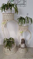 Two cream metal filigree plant stands with three potted plants and fabric squirrel doorstop