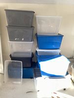 Stack of plastic storage bins in dark gray, white translucent, and blue colors with lids included.