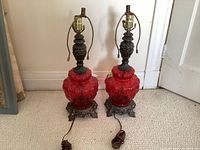 Full view of the matching pair of red glass and metal table lamps side by side on carpeted floor.