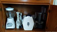 Oster blender, Braun immersion blender, Proctor Silex waffle maker, Oster food processor base inside cabinet