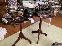 Pair of vintage wood pedestal tables shown with items on top, round tops and tripod bases visible.
