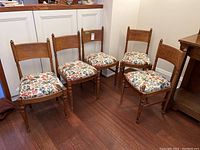 Five wooden chairs with floral upholstered seats arranged together on a wooden floor.