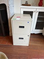 Front view of white metal two drawer file cabinet with black recessed handles, showing scratches and marks on surface.