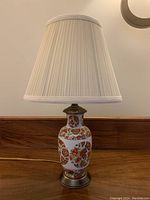 Full view of the lamp with pleated white lampshade and patterned ceramic base on wooden surface.
