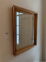Front-facing view of rectangular wall mirror with a smooth medium brown softwood frame, showing clear reflective glass and door reflection.