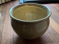 Side angle of glossy beige ceramic planter with a rounded shape and flared rim.