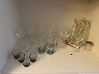 Six clear martini glasses, four shot glasses (smoky gray), three beer mugs, three glass locking bottles, clear juice glasses, small metal jar, and other items on a shelf.