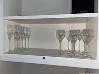 Shelved view of eight wine glasses and eight Nachtmann crystal flutes, clear glass.