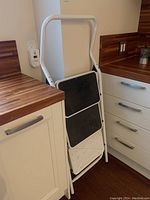 Folded 3-step ladder with white metal frame and black and white steps, showing missing tread on bottom step