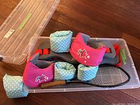 Children's swim floats, tennis racket, and plastic storage bin shown together