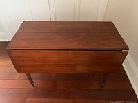 Top and side view of vintage hardwood drop-leaf table folded with one leaf down, showing rich brown finish and some wear.
