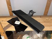 Black metal TV wall mount bracket with mounting plates and screws on wooden shelving.