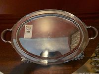 Top-down view of the oval tray on wooden surface showing handles, border and monogram