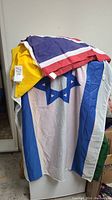 Israeli flag with visible blue Star of David and stripes on white fabric, on top a folded yellow flag.