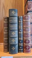 Front view showing four leather bound books with detailed gold embossing and titles visible on spines.