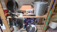 Photo showing assortment of cookware and kitchen utensils including pots, frying pan, knives, and glass bottle