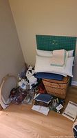 Photo showing assortment of sewing and knitting supplies including fabrics, embroidery hoops, yarn, cutting board, and woven basket hamper.