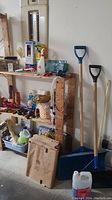 Wide view of wooden shelves with assorted home cleaning and repair products, fire extinguisher, and two snow shovels leaning against the wall.