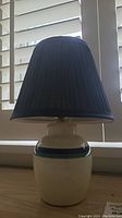 Full view of the table lamp showing the navy blue pleated lampshade and ceramic base with a blue band.