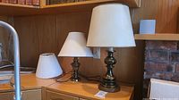 Two brass base table lamps with white shades on a wood surface
