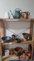 Photo showing entire wooden shelf with assorted pottery, planters, and watering cans
