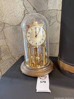 Full view of the anniversary clock showing the brass base, glass dome, and clock face with decorative brass balls.