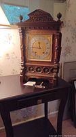 Full view of the solid wood antique mantle clock showing ornate carved details and the clock key placed on the table next to it.