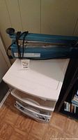 Blue impulse bag sealer placed on top of white plastic storage drawers.