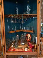 Full cabinet view showing shelves and assortment of bar accessories including glasses, decanters, ice bucket, bar mats and drink koozies.