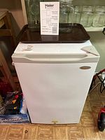 Front view of the Haier mini fridge showing clean white exterior, top freezer compartment section, with informational sticker on top.
