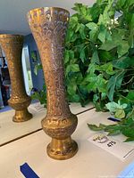 Front view of tall brass vase with detailed carving and floral patterns.