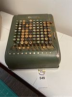 Top front view of a green Comptometer calculator showing multiple hexagonal colored keys in rows and columns, with visible rust and dirt.